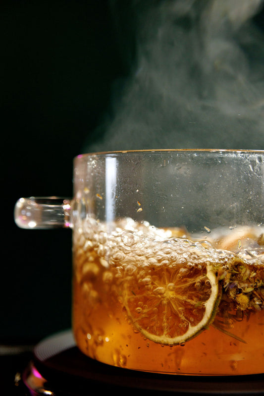 Steaming simmer pot with lemon and herbs in a clear pot against a dark background