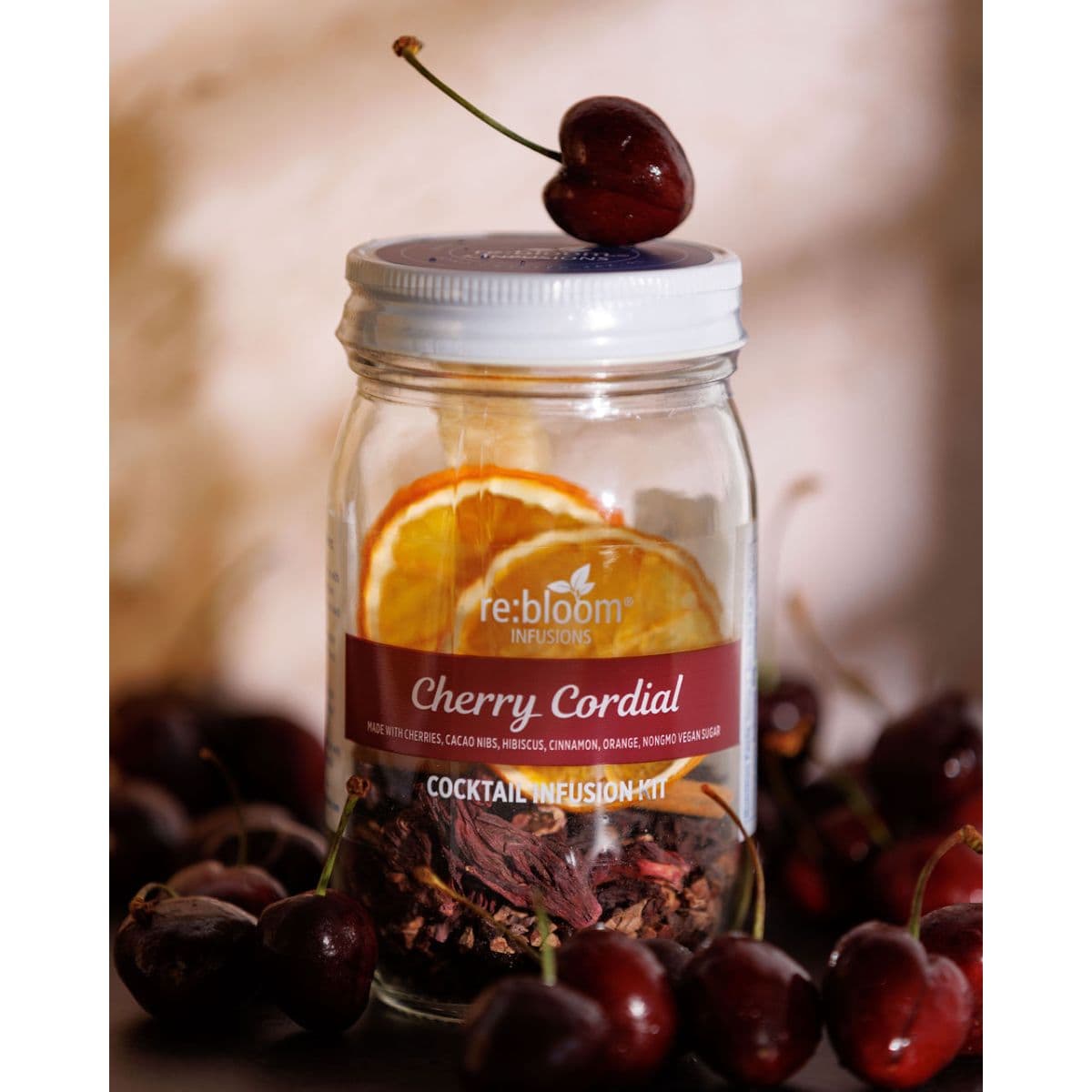Cherry Cordial cocktail infusion kit surrounded by fresh cherries with citrus slices and a cherry balanced on top of the jar lid.