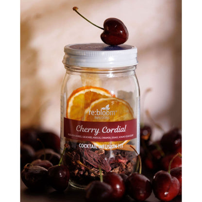 Cherry Cordial cocktail infusion kit surrounded by fresh cherries with citrus slices and a cherry balanced on top of the jar lid.