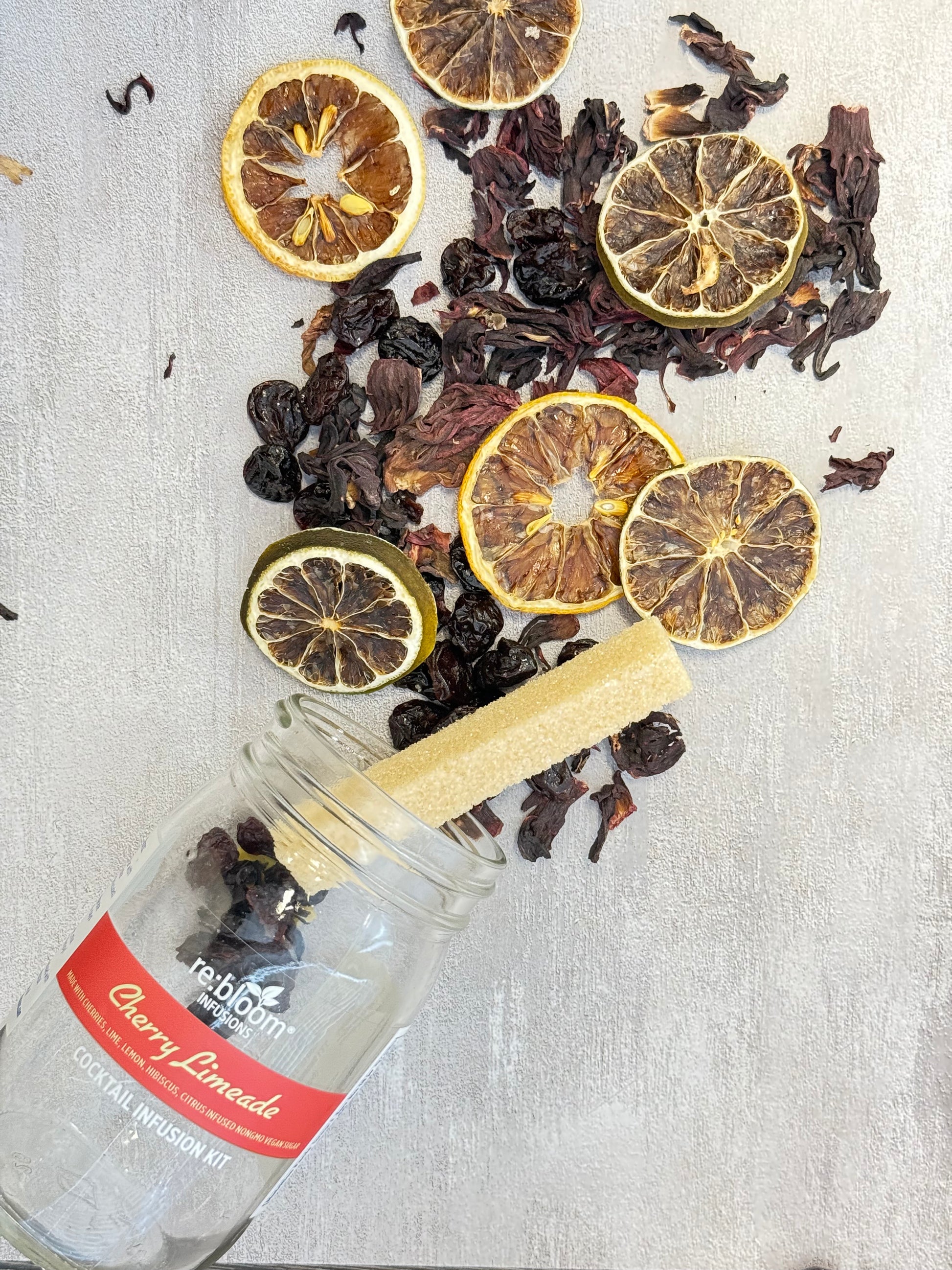 Dried lemon slices and herbs with a cherry limeade bottle on a textured surface
