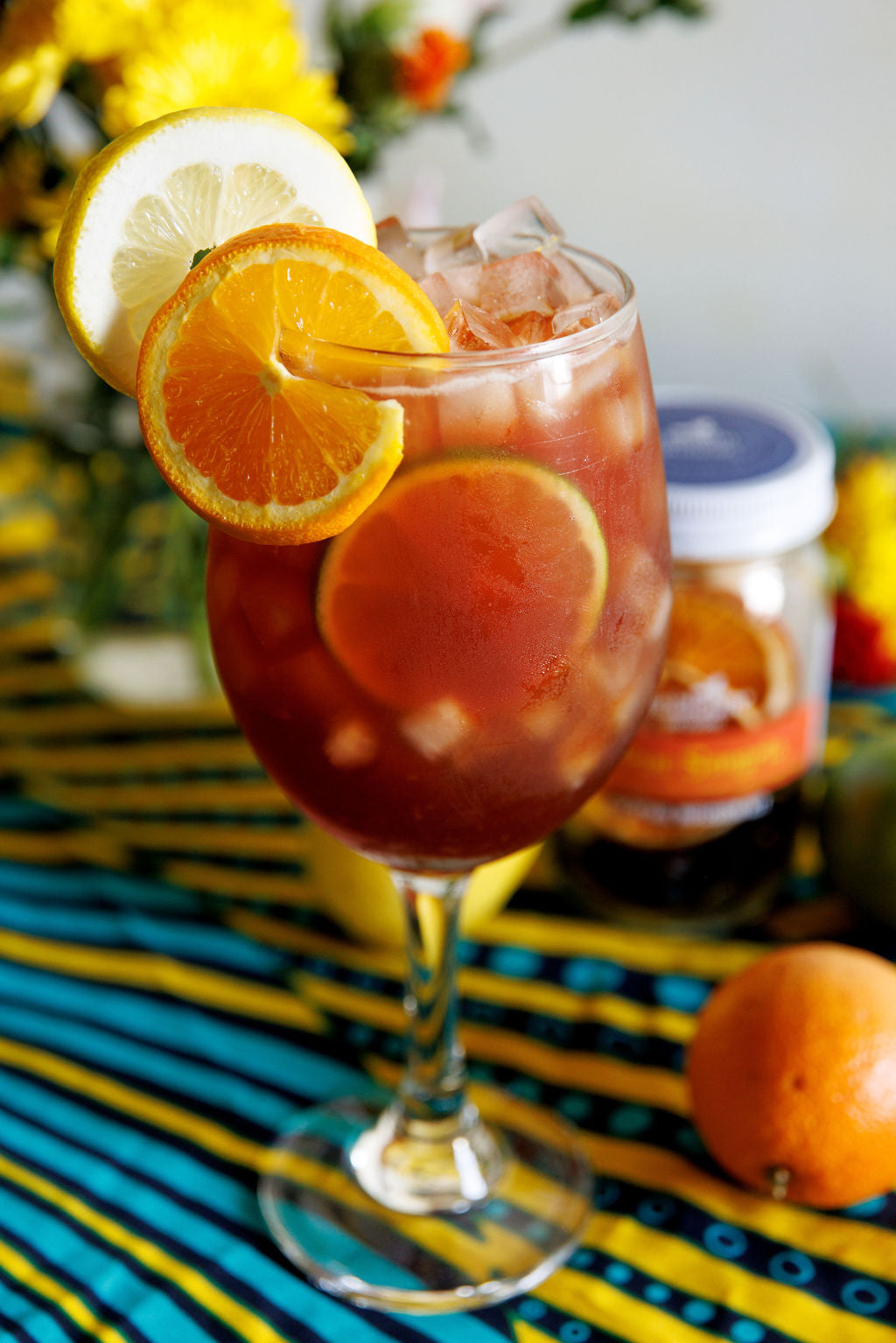 Glass of sangria with sliced oranges and lemons on a colorful striped surface.
