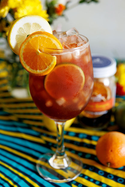 Glass of sangria with sliced oranges and lemons on a colorful striped surface.