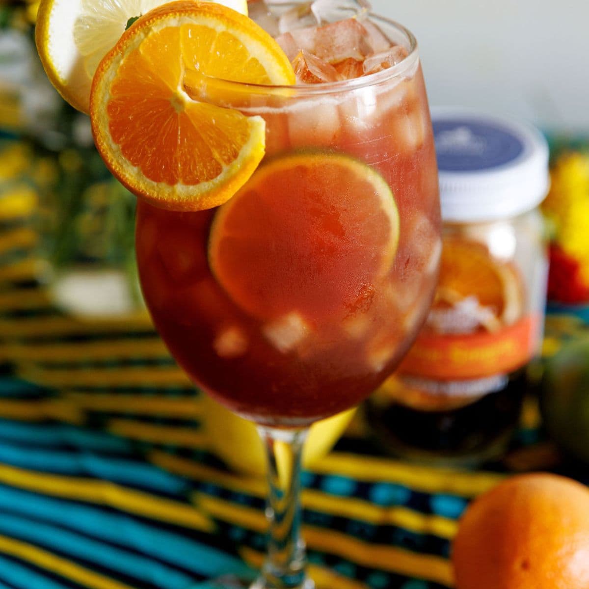 Glass of sangria with sliced oranges and lemons on a colorful striped surface.