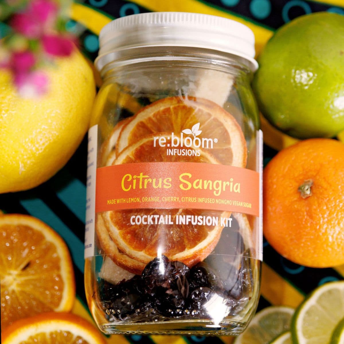 Jar of re:bloom Citrus Sangria cocktail infusion kit surrounded by citrus fruits on a colorful background