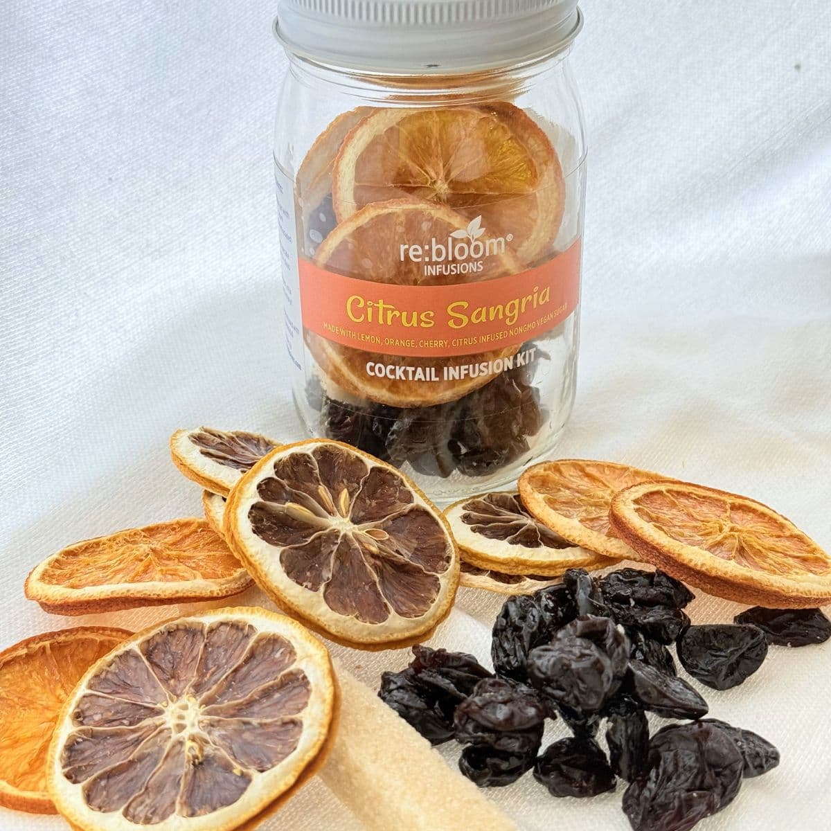 Jar of 'Citrus Sangria' cocktail infusion kit with dried citrus slices and prunes on a white background