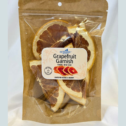 A package of ReBloom Grapefruit Garnish edible garnishes inside a brown kraft paper stand-up pouch, showing dried grapefruit slices visible through the clear plastic.