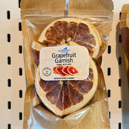 A package of Rebloom Grapefruit Garnish, featuring dried grapefruit slices inside a brown kraft paper bag with a clear plastic window and a white product label.