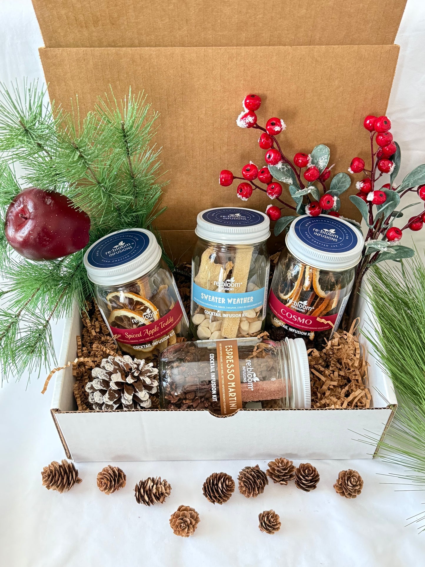 Open gift box with Christmas decorations and jars of treats on a white surface.