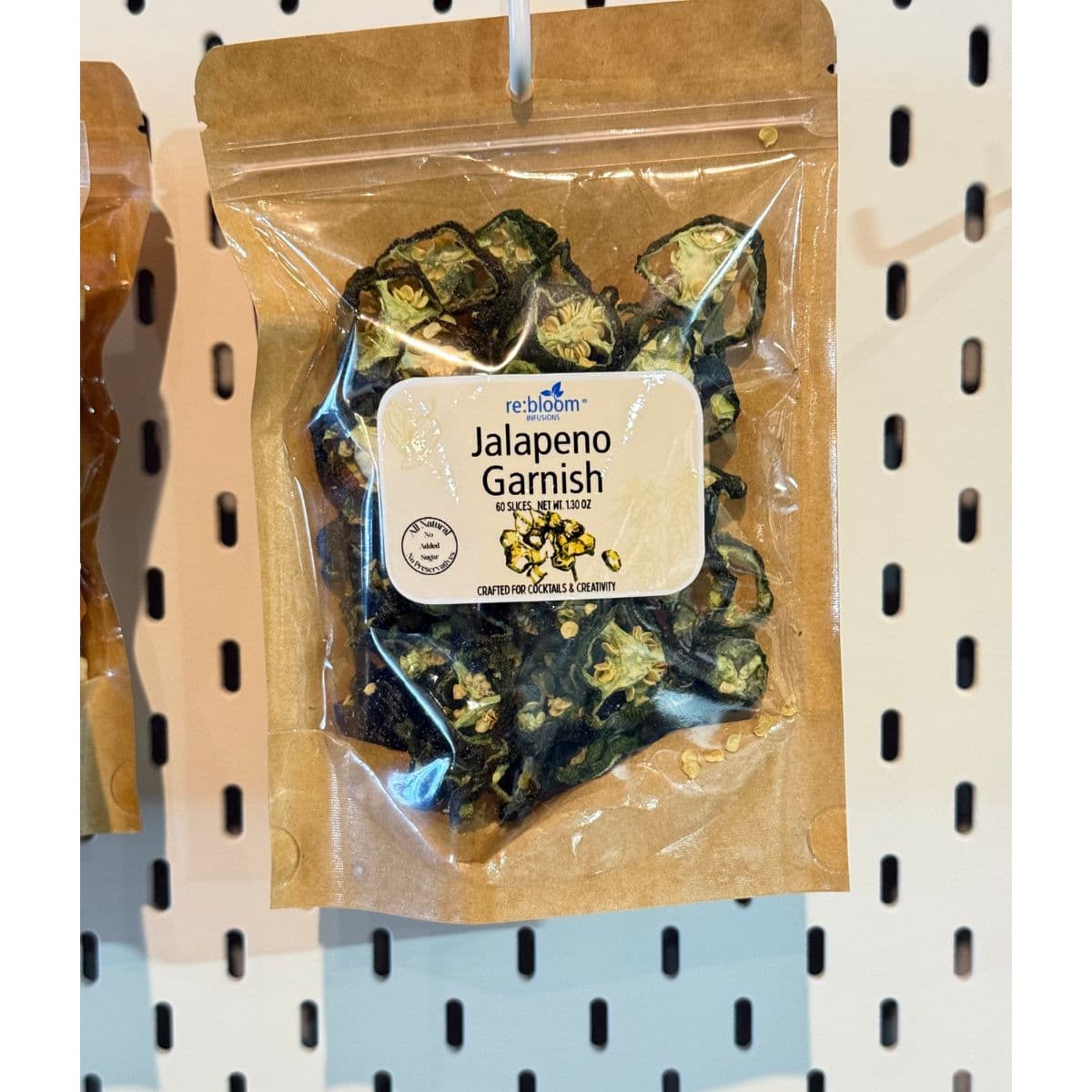 Packaged jalapeño garnish with visible re:bloom Infusions label hanging on a pegboard display.