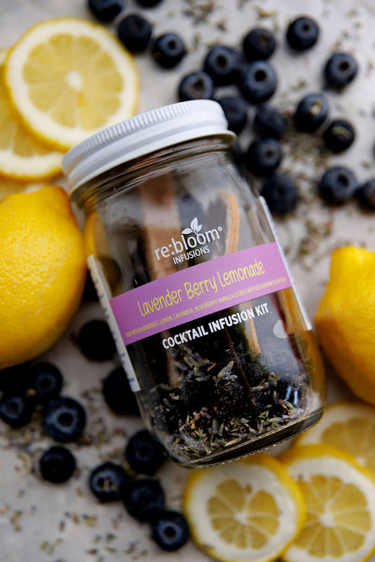A complete lavender berry lemonade dehydrated cocktail infusion jar with fresh lemons and blueberries around it.