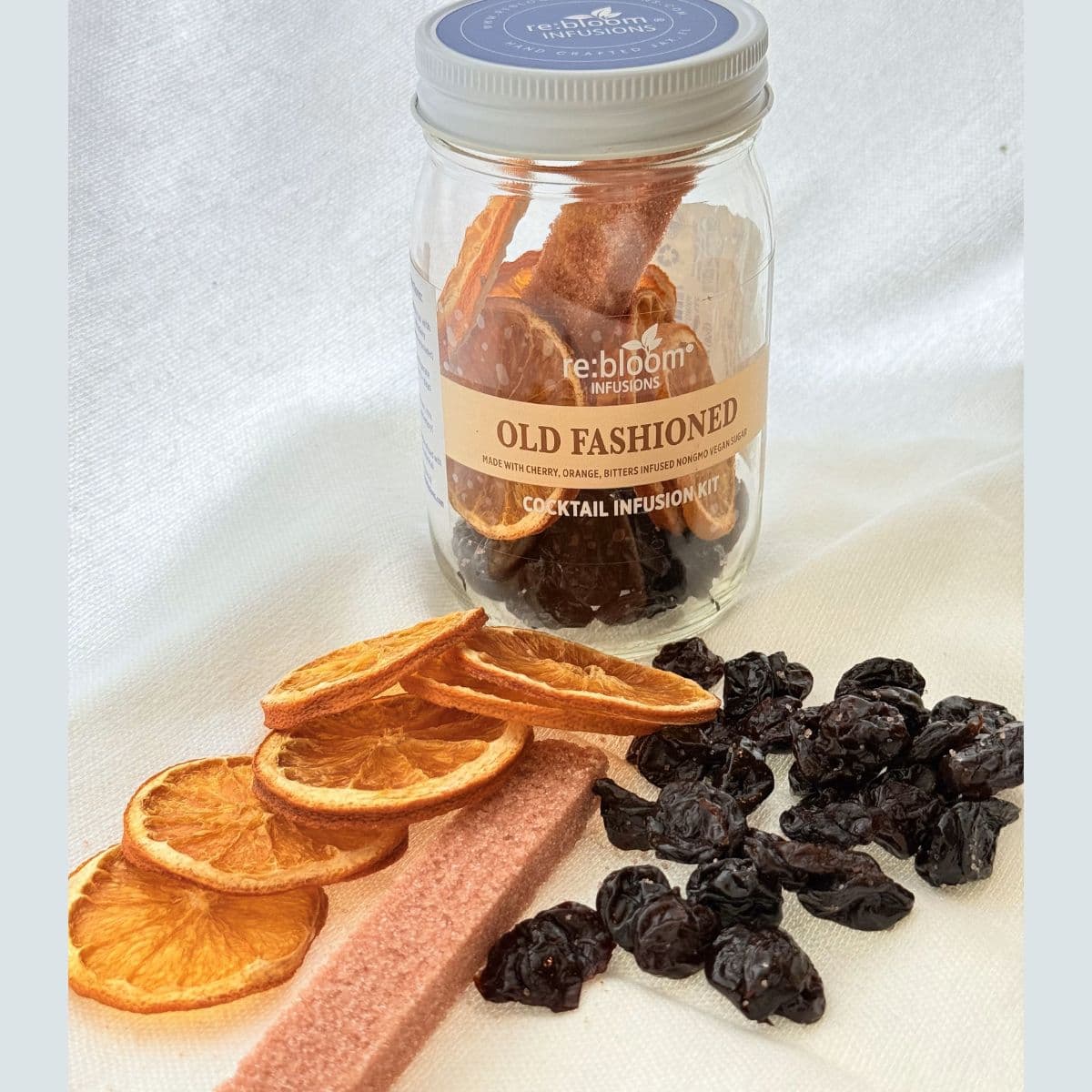 Jar of Old fashioned cocktail infusion mix with dried oranges, cherries, and a bitters-infused infused sugar on a white background.