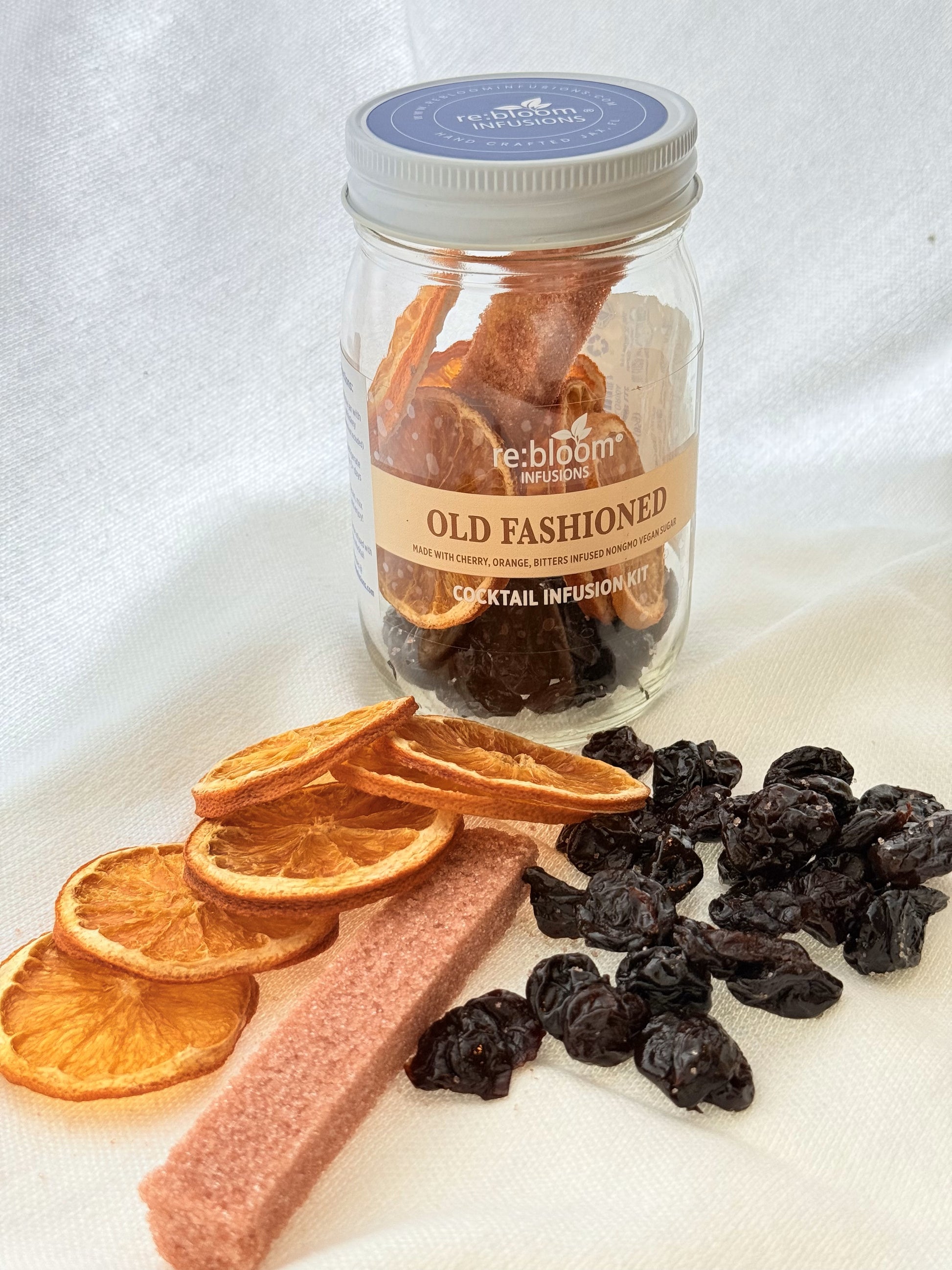 Jar of Old fashioned cocktail infusion mix with dried oranges, cherries, and a bitters-infused infused sugar on a white background