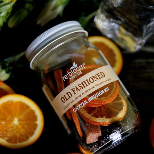 Old  Fashioned cocktail infusion kit with oranges and greenery on a dark surface.