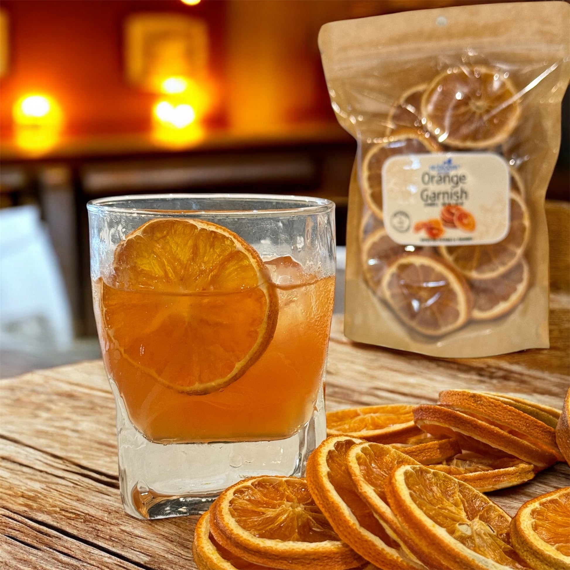 Glass of orange cocktail with dried orange slices and a package labeled 'Orange Garnish' on a wooden surface.