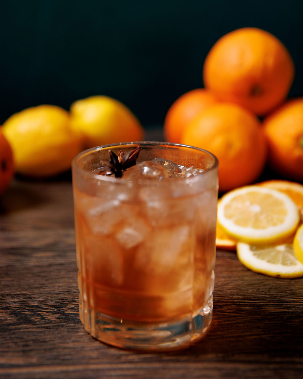 Sazerac cocktail surrounded by fresh citrus on a dark wooden background