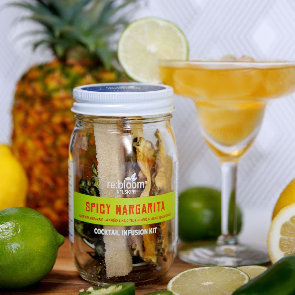 Spicy Margarita cocktail infusion kit with a glass of margarita, pineapple, lemon, and lime in the background.