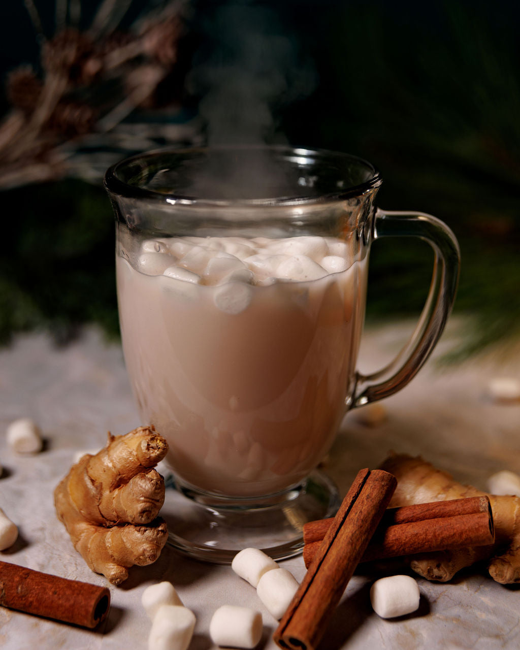Sweater Weather Cocktail hot in a clear glass mug surrounded by marshmallow ginger and cinnamon