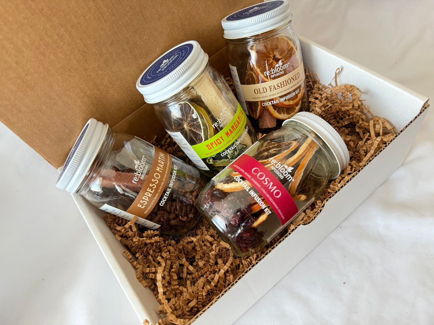 Four jars of best selling infusion cocktail kits in a gift box with brown crinkle paper