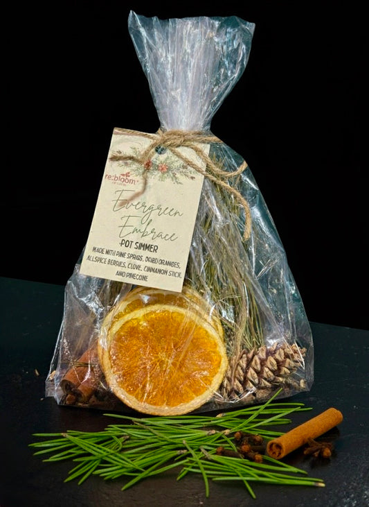 Pouch of potpourri simmer pot kit with cinnamon sticks, pine cones, and orange slices on a dark surface.